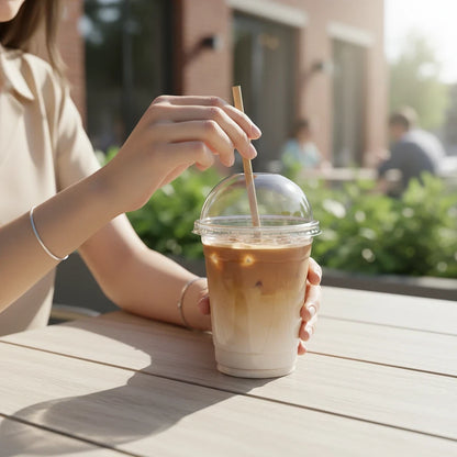 Food Packaging Direct clear PET plastic dome lid on a smoothie cup with a straw, held by a person at an outdoor cafe.